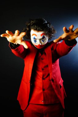 man in joker face makeup showing hands, in red formal with scary eyes , image