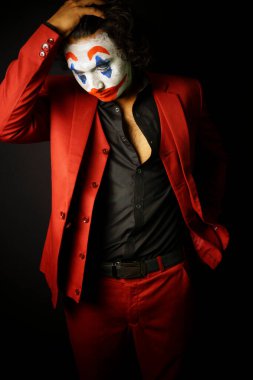 man in joker face makeup looking down in sad pose, in formal outfit