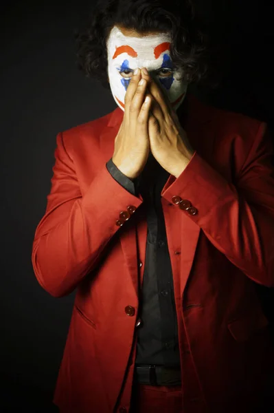 man in joker face makeup , hands on face in formal outfit