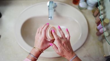 Yaşlı kadınların eli cilt bakımı ve su içmesi için şişeden krem alıyor.