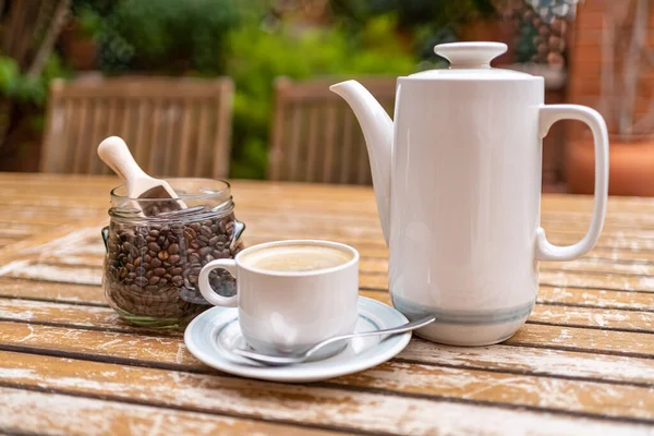 Coffee set with coffee maker, cup and glass jar with coffee beans on a wooden garden table
