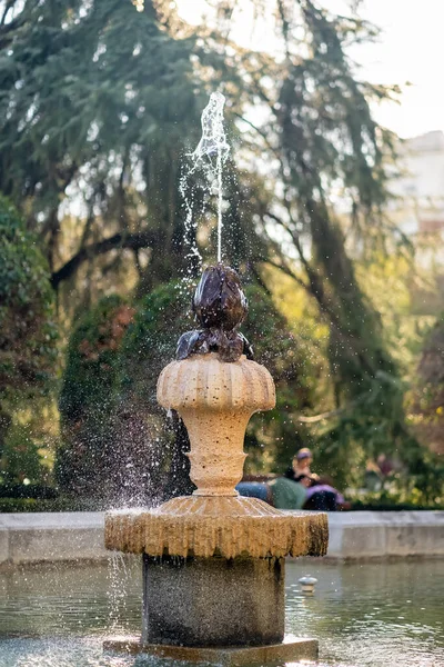 Bir parkın eski çeşmesi arkasında güneş ışığı olan jetleri fırlatıyor, El Retiro Madrid.