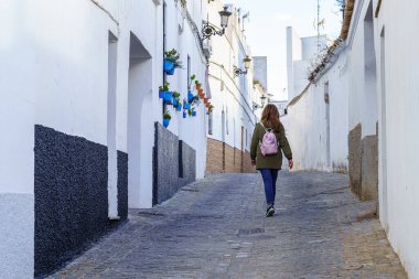 Cadiz 'in pitoresk şehri Medina Sidona' nın dar sokaklarında yürüyen sırtı dönük bir kadın turist.