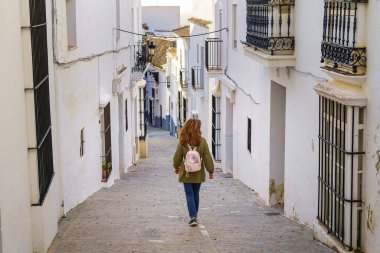 Beyaz evlerin ve pencerelerdeki metal parmaklıkların olduğu tipik bir Endülüs köyünde yürüyen kadın, Medina Sidonia, Cadiz