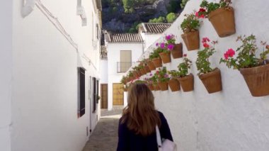Duvarlarından sarkan beyaz evler ve saksılarla dar bir sokakta yürüyen kadın, Grazalema, Cadiz