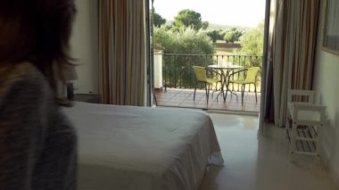 Elinde bavul olan bir kadın otel odasına geliyor ve yorgun bir şekilde yatağa uzanıyor.