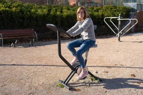 Senior woman riding a stationary bike in a public city park to keep fit