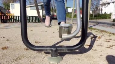 Kadınların bacakları halka açık bir parkta jimnastik aletleri üzerinde salınım egzersizleri yapıyor.