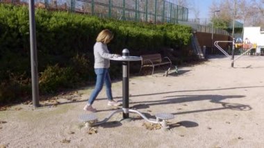 Olgun bir kadın, vücudun esnekliğini ve gücünü arttırmak için halka açık bir parkta jimnastik yapıyor.