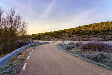 Donmuş kırsal kesimde soğuk bir kış gününde gün batımında buzlu bir yol.