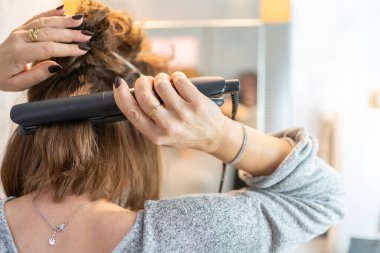Woman fixing her hair in front of the mirror, using a hair straightener