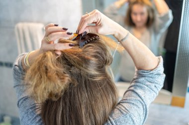 Woman in front of the mirror fixing her hair with both hands making a ponytail