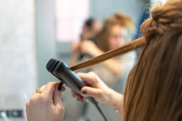 Detail of a hair straightener while being used by a woman in front of the mirror in her bathroom
