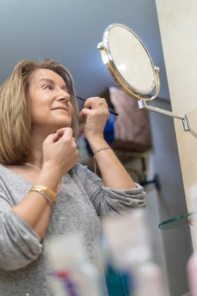 Mature white woman applying beauty treatments in front of the mirror of her bathroom.