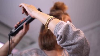 Detail of a hair straightener while being used by a woman in front of the mirror in her bathroom