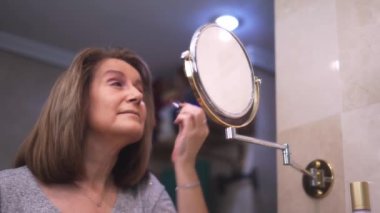 Mature white woman applying beauty treatments in front of the mirror of her bathroom.