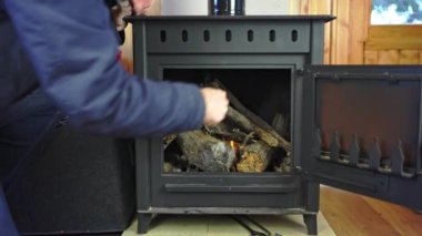 Man lighting the fire inside a rustic cast iron stove to heat the house