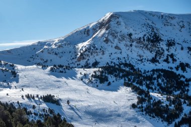 Skiers gliding down the slopes of the high snowy mountains on a sunny day, Pyrenees, Grandvalira, Andorra