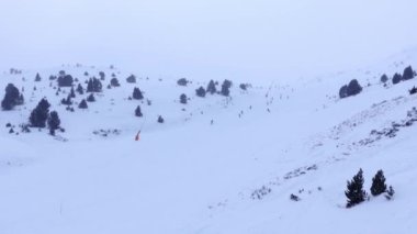 Bulutlu ve kar fırtınalı bir günde kayak yamacından inen kayakçılar, Andorra, Grandvalira