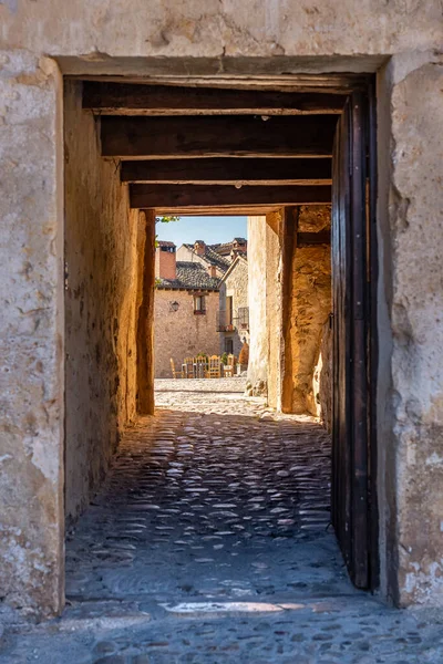 Narrow passageway and alley leading to a square with wooden tables and chairs in the sun, Pedraza, Segovia, Spain