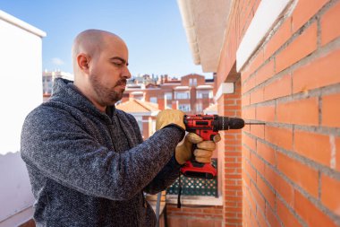 Young white man DIY with a drilling machine on the wall of his terrace