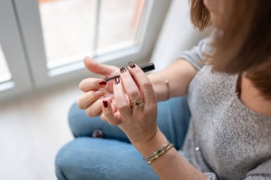 Yaşlı bir kadın pencerenin önünde tırnaklarını boyuyor. Dışarıdaki ışığın içeri girdiği yerde.