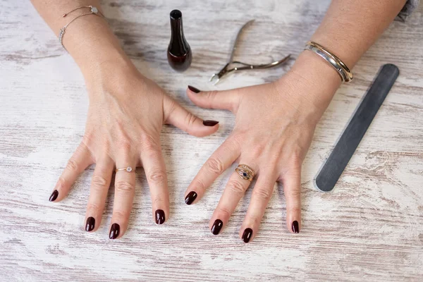 Womens hands with nails freshly painted dark red and instruments used for manicure