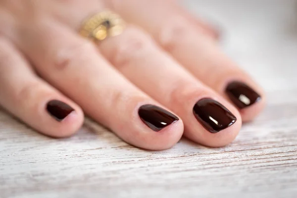 White womans hand with nails freshly painted dark red on a wooden table