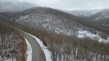 Karlı bir ormanın hava aracı görüntüsü yüksek dağlar arasında bir yol rüzgarı, Somosierra, İspanya