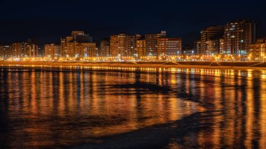 Geceleri deniz suyundaki ışık ve binaların yansımalarıyla dolaşın, Gijon, Asturias.