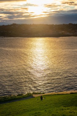 Sakin ve sakin bir günde denizin dalgalarında altın yansımalarıyla Gijon şehrinin üzerinde güzel bir gün doğumu.
