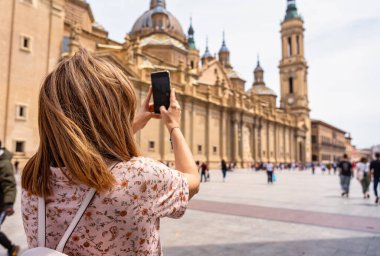 Turist kadın cep telefonuyla Zaragoza, İspanya 'daki katedral bazilikasına fotoğraf çekiyor.