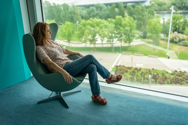 stock image Woman sitting in a relaxed armchair and contemplating the landscape from a large window of the room