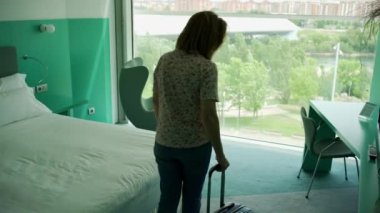 Yetişkin bir kadın otel odasına gelir ve dinlenmek için bir koltuğa oturur.