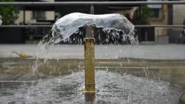 Yavaş çekimde su jeti olan küçük bir çeşme ve arkamızdan dikkatsiz insanlar geçiyor
