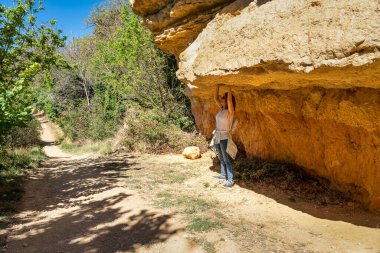 Orman yolunda, Anento, Zaragoza 'da büyük bir taşın oluşturduğu gölgede yürüyen bir kadın.