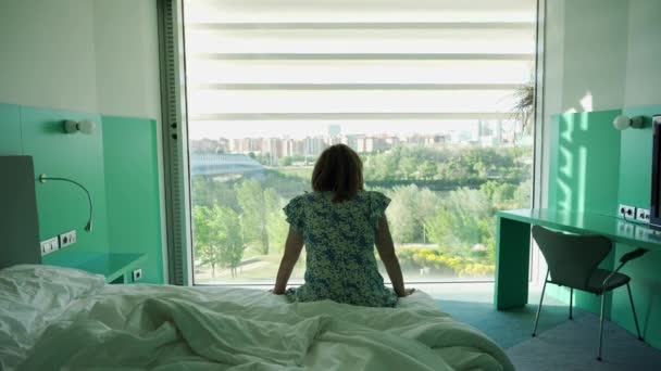 Sırtı Yatakta Oturan Kollarını Açıp Pencereden Manzarayı Seyreden Bir Kadın — Stok video