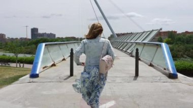 Şehrin rüzgarlı bir gününde, modern bir köprüde gezinen kadın, Zaragoza