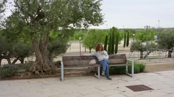 萨拉戈萨 一个刮风的日子 一个女人坐在公园的木制长椅上 — 图库视频影像