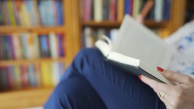 Bir kadının kitap okuduğu ve yanında bir rafla sayfaları çevirdiği yakın plan.