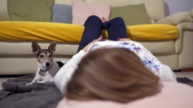 Kitap okuduktan sonra köpeğiyle oynarken yerde yatan beyaz kadın.