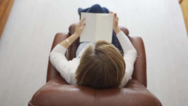 一个女人坐在一张舒舒服服的扶手椅上看书的头像 — 图库视频影像