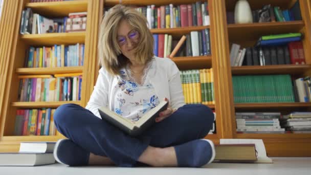 彼女の後ろに多くの本が開かれ 本棚と床の上に座っている白人女性 — ストック動画