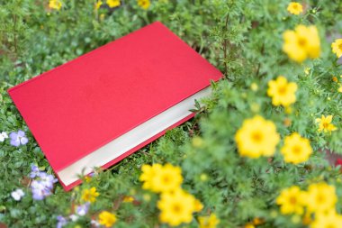 Yeşil bitkiler ve sarı ve mavi çiçekler üzerine kırmızı kitap