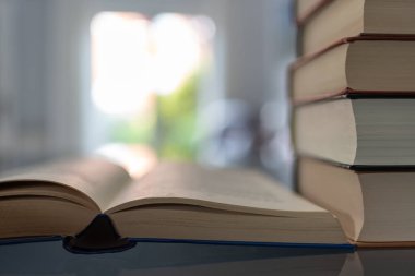 Arka planda ışık parıltısı olan açık bir kitabın yanına istiflenmiş kitaplar. Kopyalama alanı olan fotoğraf