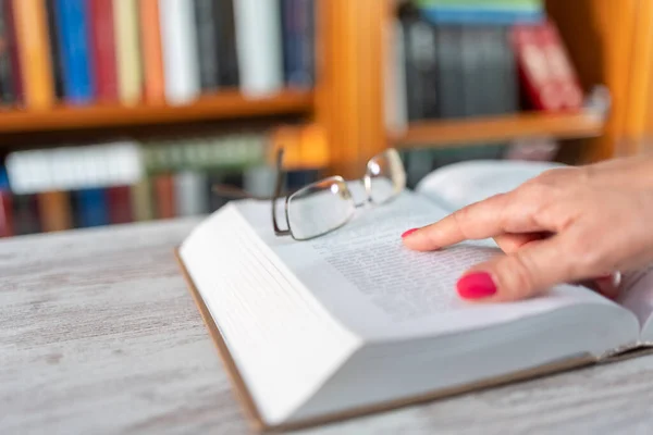 Book on wooden table with a womans hand that points to the written text
