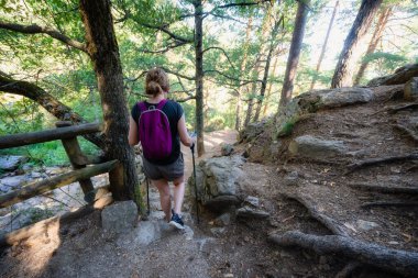 Madrid, Sierra de Guadarrama 'da büyük kayalar ve yüksek ağaçlar arasında bir patikada yürüyen bir kadın.