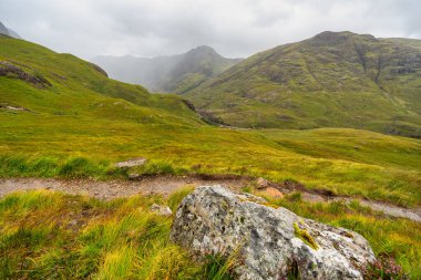 İskoçya 'daki Glencoe Vadisi' nde sis kaplı yeşil dağlar ve yürüyüş yolları