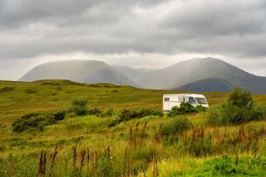 Karavan, İskoçya 'daki Glencoe Vadisi' nin yanındaki yeşil çayırların arasına park etmiş.