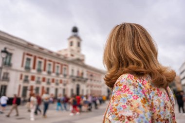 Sırtı dönük bir turist kadın Madrid 'deki Puerta del Sol binalarının saat kulesine bakıyor.